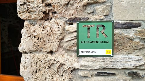 Cartel verde de alojamiento rural para la casa L'Orri Rectoria Nova en Campelles, montado en pared de piedra