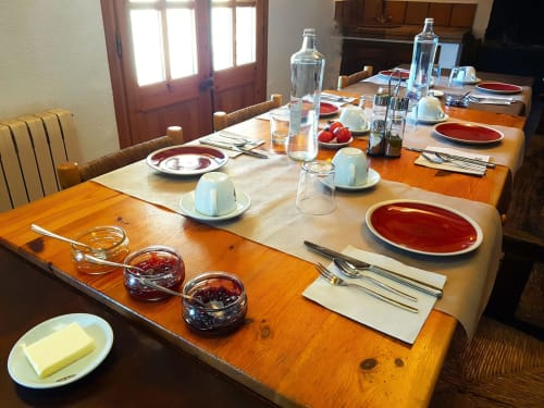 Mesa de comedor formal dispuesta para huéspedes en la casita L'Orri Rectoria Nova de Campelles con cubiertos, vasos de agua y detalles rojos