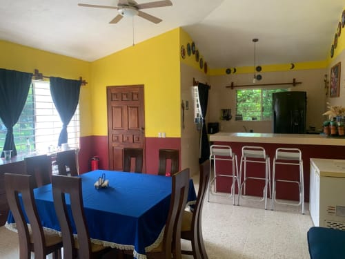 Comedor y cocina de la villa Casa Leticia con mesa azul, paredes amarillas y vistas al jardín en La Morada, Monte Gordo