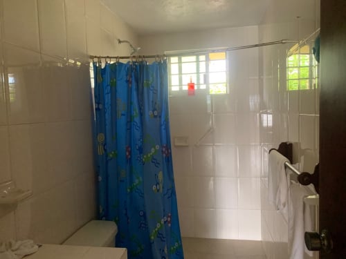 Baño luminoso con cortina de ducha azul, azulejos blancos y ventana en villa Casa Leticia, Monte Gordo