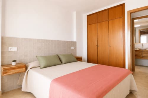 Dormitorio moderno en Riurau Home Calpe con armario de madera, apartamento con vistas al mar, ropa de cama blanca y coral