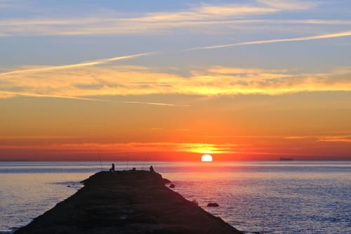 Atardecer espectacular sobre el Mar Mediterráneo desde Museros, España con pescadores silueteados en las rocas