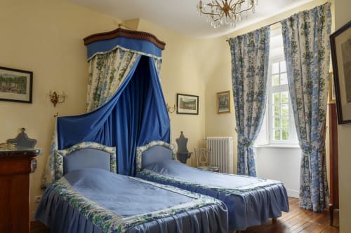 Chambre historique du Château de Servigny avec lit à baldaquin bleu, murs jaunes et mobilier d'époque à Yvetot Bocage.
