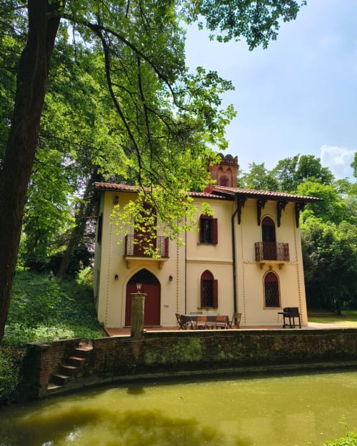 Veneto Villa B&B in Sant'Agostino: cream and red villa with tower reflected in moat, surrounded by lush green trees