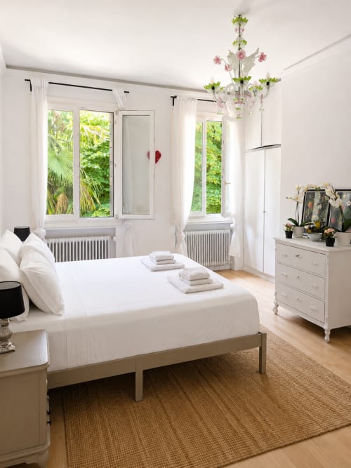 Bright bedroom at Veneto Villa B&B in Sant'Agostino with white linens, garden views, chandelier, and wooden floors.