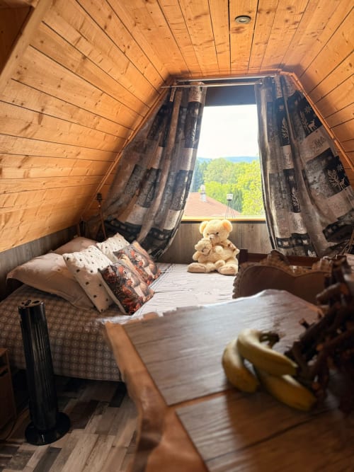 Chambre douillette en bois aux Cabanes des Marchous avec vue montagne, lit avec oreillers, peluche et forêt