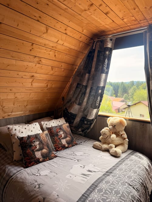 Chambre douillette en bois avec vue sur les montagnes, oursons, coussins à motifs et rideaux foncés aux Cabanes des Marchous
