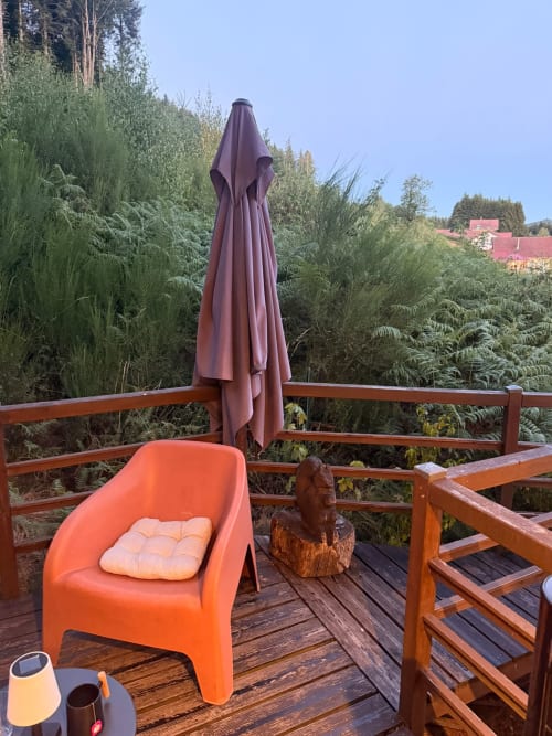 Chaise orange avec coussin sur la terrasse en bois du gîte Les Cabanes des Marchous, parasol bordeaux, vue sur la forêt