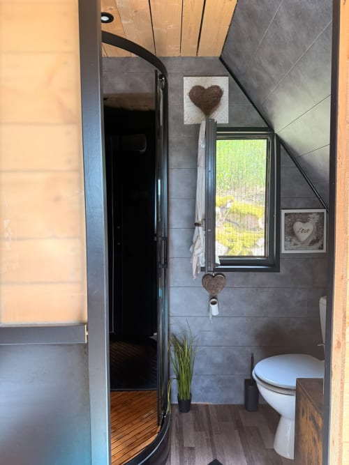 Salle de bain moderne du gîte Les Cabanes des Marchous avec douche, toilettes, vue sur fenêtre et décors cœurs