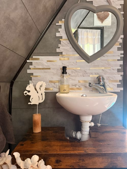 Miroir en forme de cœur au-dessus d'un lavabo blanc dans la salle de bain de la cabane L'Écureuil aux Cabanes des Marchous, France