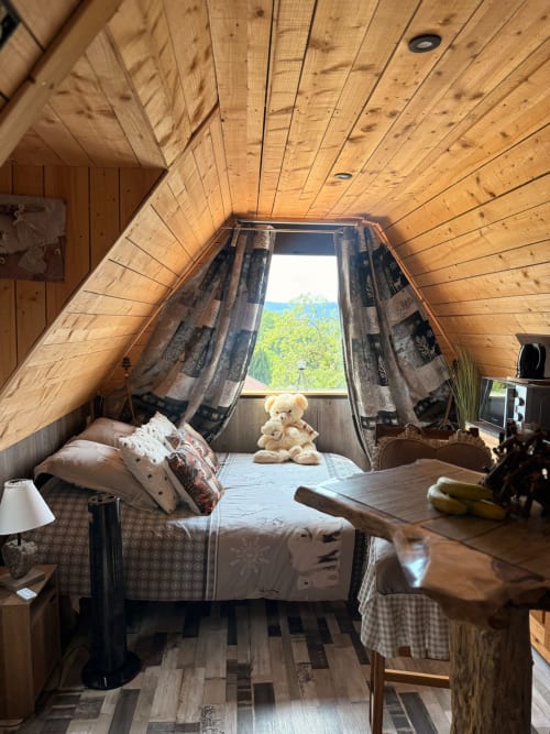 Chambre cosy en chalet A-frame aux Cabanes des Marchous, avec plafond bois, vue montagne par grande fenêtre et peluche