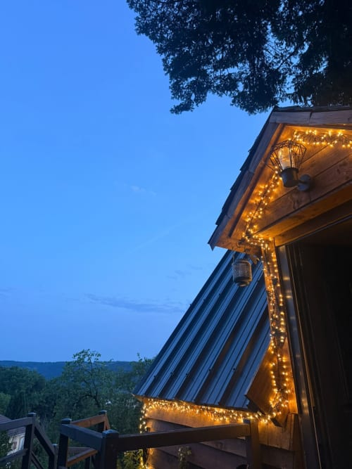 Vue nocturne du gîte Les Cabanes des Marchous illuminé de guirlandes lumineuses chaleureuses, paysage montagneux visible
