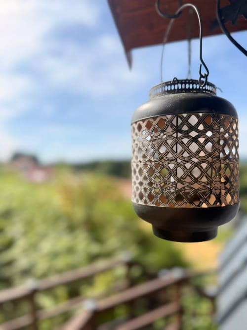 Lanterne décorative suspendue au toit d'une cabane dominant une campagne verdoyante aux Cabanes des Marchous
