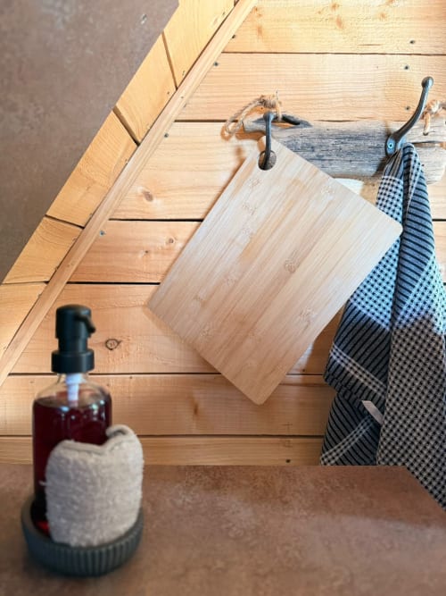 Planche à découper en bois, torchons de cuisine et distributeur de savon sur un plancher en bois au gîte Les Cabanes des Marchous