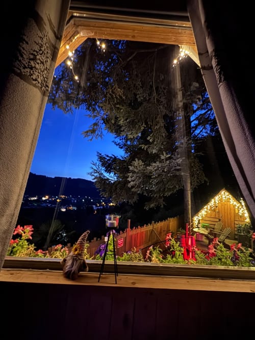 Vue depuis la fenêtre de la Cabane Marmotte au crépuscule : jardin orné, chalet illuminé et paysage montagneux