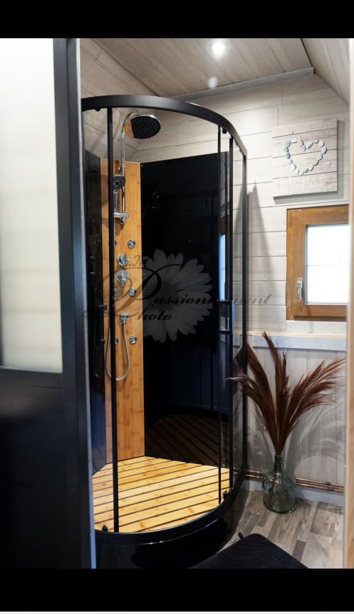 Cabine de douche moderne en bois avec cadre noir et pommeau de douche pluie à la Cabane Marmotte des Cabanes des Marchous