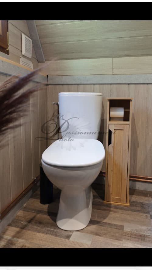 Toilettes blanches modernes avec meuble de rangement en bois dans la salle de bains du gîte Cabane Marmotte, décorée de panneaux de bois