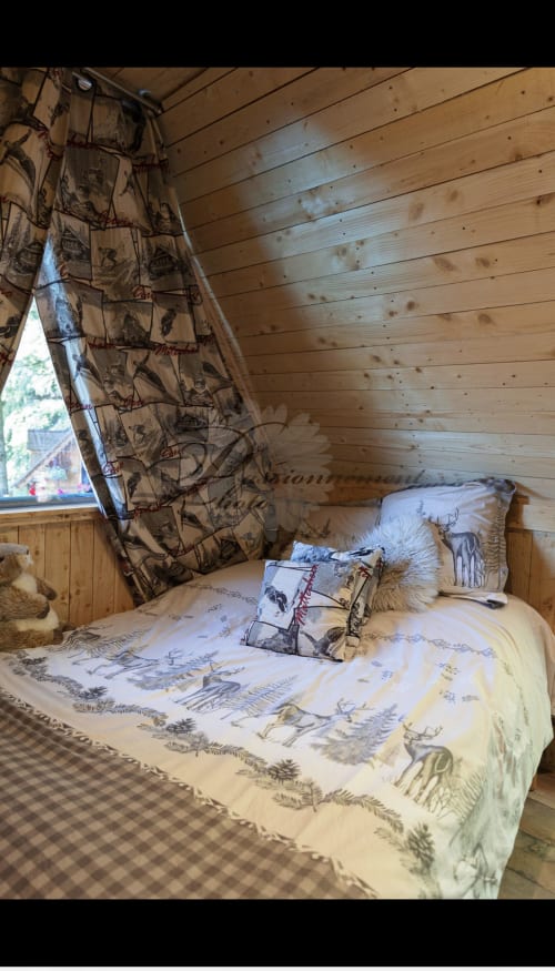 Chambre douillette aux Cabanes des Marchous avec literie et rideaux à thème animalier, murs en bois naturel
