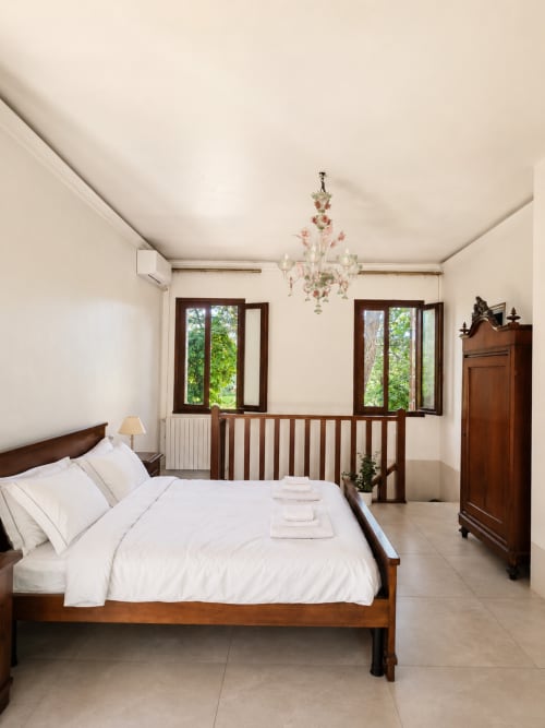 Elegant bedroom at Veneto Villa Lake House with wooden bed, white linens, chandelier, and lake views through windows