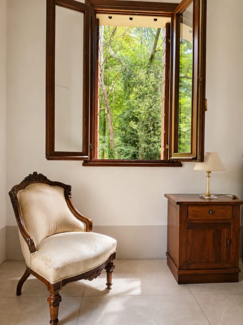 Elegant room at Veneto Villa with cream upholstered chair, wooden furniture, and open doors overlooking lush garden views