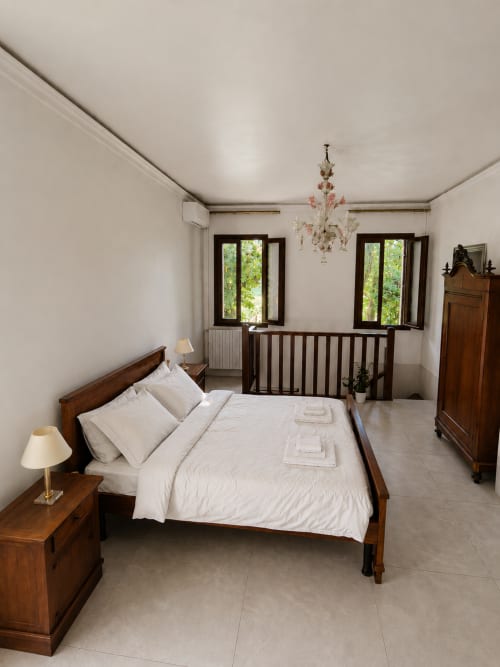 Elegant bedroom in Veneto Villa Lake House with wooden bed, cream bedding, chandelier, and lake views through French doors