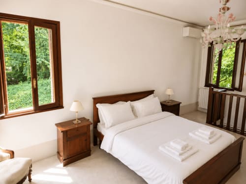 Bright bedroom at Veneto Villa Lake House with wooden bed, white linens, twin nightstands, and views of lush grounds near