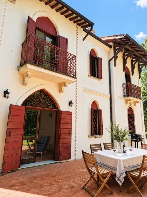 Veneto Villa terrace with red wooden doors, arched windows, dining table, and wooden chairs in Sant'Agostino, Italy