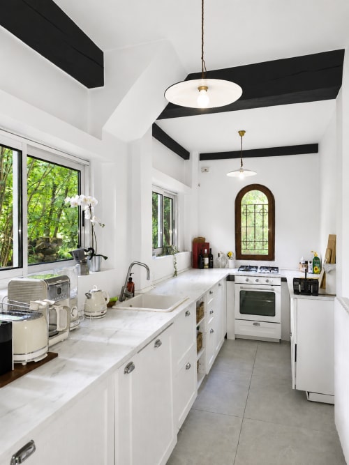 Modern white kitchen with black ceiling beams, marble countertops, stainless steel appliances, and garden views at Veneto