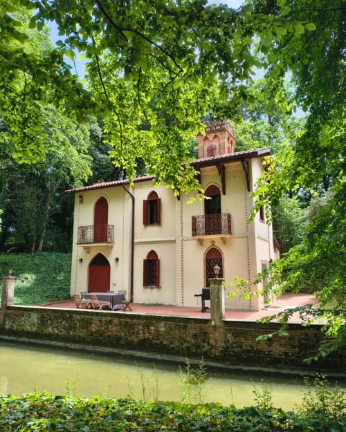 Veneto Villa Lake House, a cream-colored Italian villa with red doors and brick tower, surrounded by lush greenery and