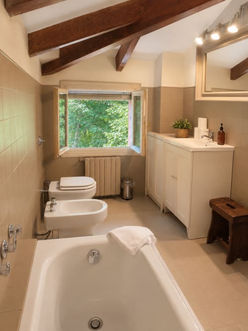 Spacious bathroom in Garden Loft at Veneto Villa with bathtub, bidet, toilet, sink, and garden view through large window