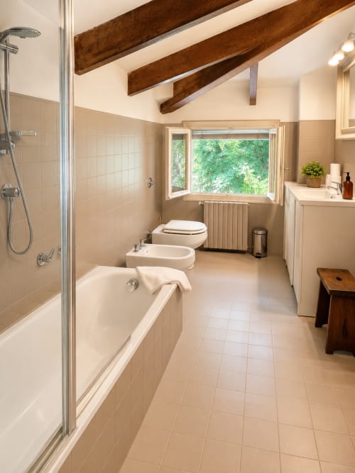 Spacious bathroom in Garden Loft apartment at Veneto Villa B&B with bathtub, shower, bidet, and garden view window