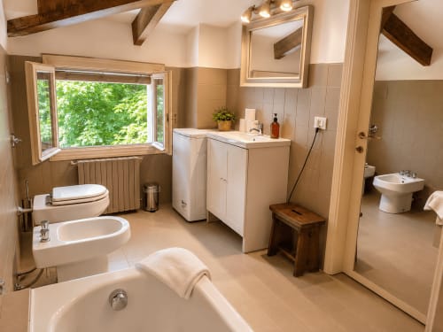 Spacious bathroom in Garden Loft apartment at Veneto Villa B&B, featuring soaking tub, bidet, dual sinks, and garden view
