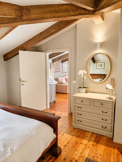 Rustic loft bedroom at Veneto Villa with exposed beams, wooden floors, cream dresser, oval mirror, and open living area at