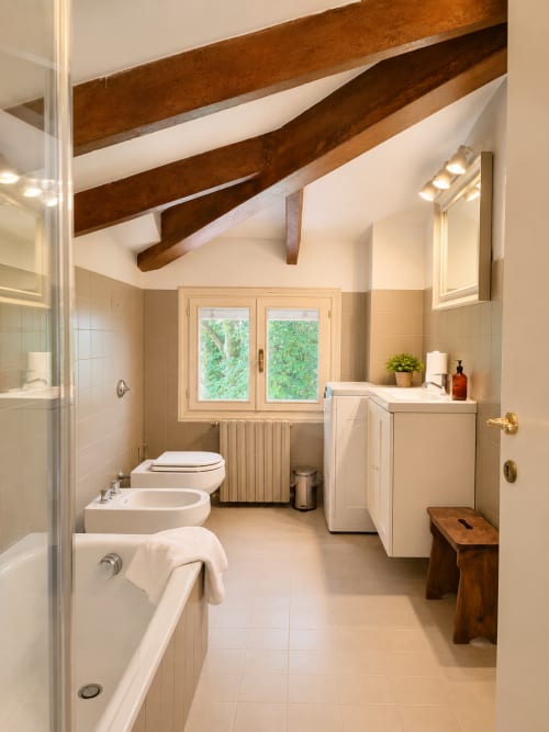 Garden Loft bathroom at Veneto Villa with exposed beams, bathtub, bidet, sink, and garden view windows