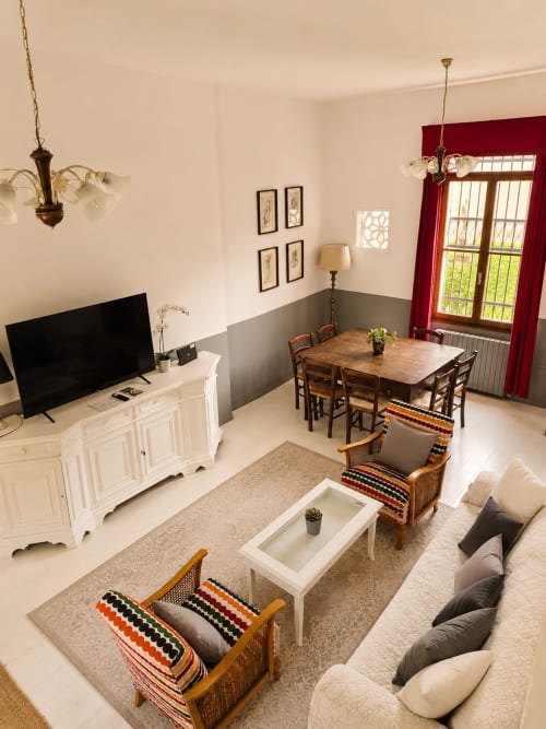 Bright living room at Veneto Villa with dining table, comfortable seating, TV, and garden views through red curtains