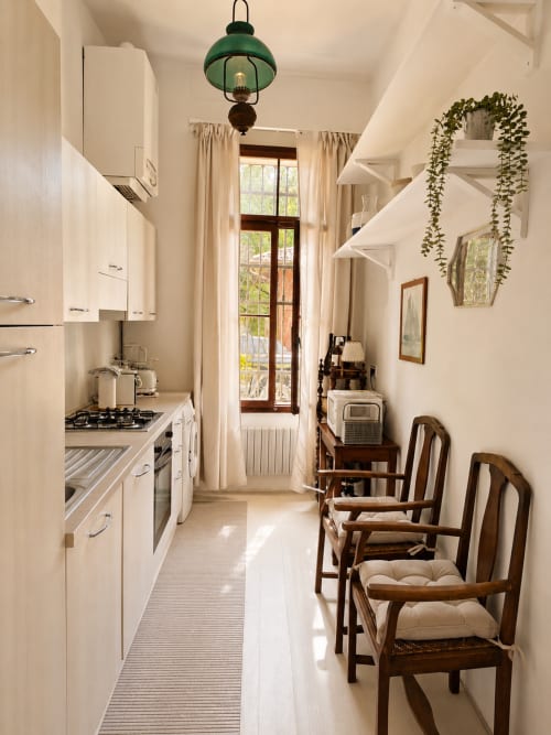 Narrow galley kitchen at Veneto Villa's Wisteria Lodge with white cabinetry, green pendant light, and garden views through