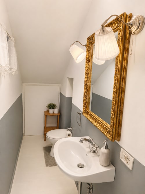 Elegant bathroom at Veneto Villa with curved sink, gold-framed mirror, dual sconces, and gray half-wall paneling