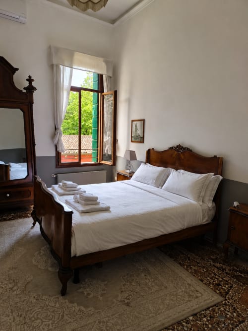 Elegant bedroom at Veneto Villa with wooden bed, white linens, garden view from open doors, and classic Italian decor in