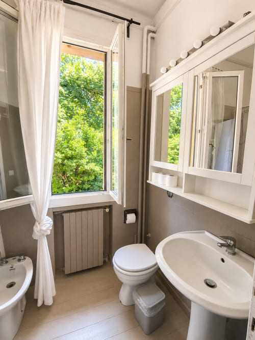 Modern bathroom at Veneto Villa with pedestal sink, toilet, mirrored cabinet, and garden view window in Sant'Agostino