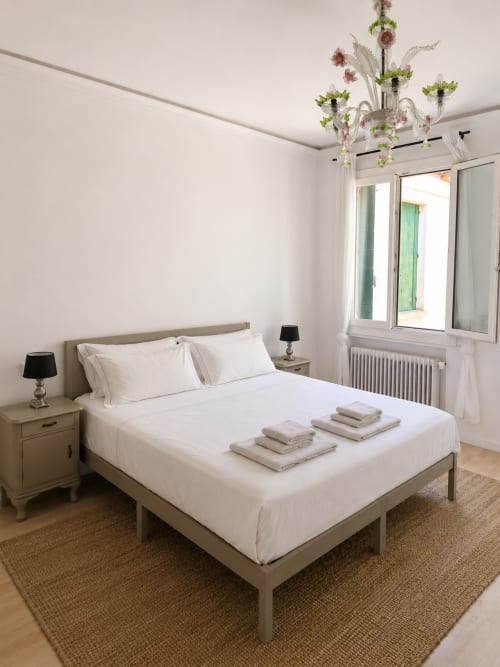 Bright bedroom with white linens, garden view windows, and decorative chandelier at Veneto Villa B&B in Sant'Agostino