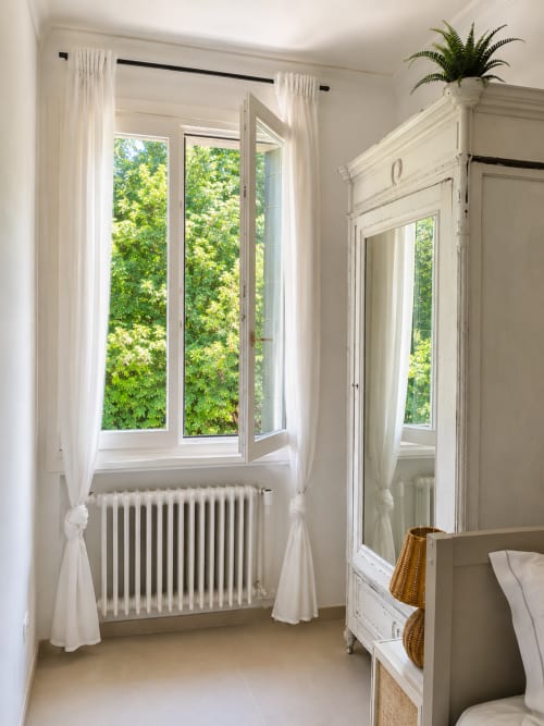 Bright bedroom at Veneto Villa with large garden-view windows, white curtains, radiator, and antique wardrobe in