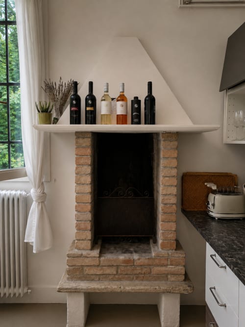 Rustic fireplace with wine bottles displayed on white mantel in Veneto Villa Garden Lodge apartment, Sant'Agostino PD Italy