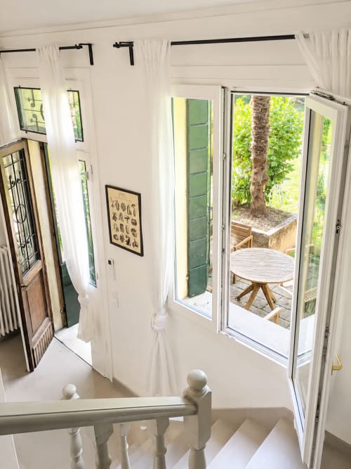 Bright hallway with white curtains and stairs leading to garden patio at Veneto Villa Garden Lodge in Sant'Agostino, Italy