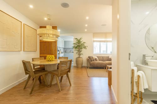Sea'Ya Cascais apartment living area with dining table, wooden chairs, pendant lamp, sofa, and kitchenette in warm neutral
