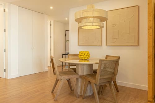 Modern dining area in Sea'Ya Cascais apartment with round wooden table, rattan chairs, and pendant light fixture above yellow