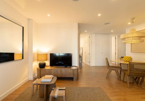 Modern apartment living room at Sea'Ya Villas in Cascais with wooden furniture, dining area, TV, and warm lighting