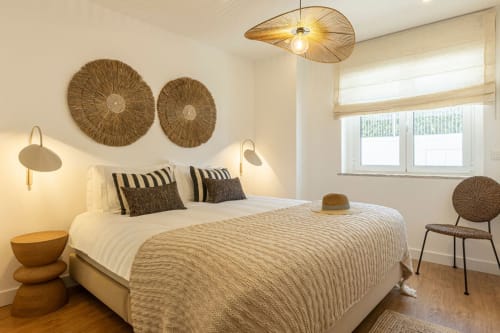 Bright modern bedroom at Sea'Ya Cascais with neutral tones, woven wall art, pendant lighting, and striped bedding in Cascais.