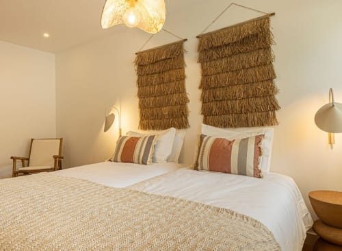 Modern bedroom at Sea'Ya Villas Cascais with two beds, striped pillows, woven wall hangings, and minimalist décor with warm