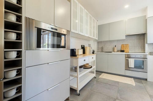 Modern kitchen in Sea'Ya Cascais apartment with white cabinetry, stainless steel appliances, and open shelving displaying