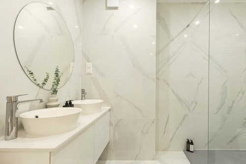 Modern marble bathroom at Sea'Ya Cascais with dual sinks, round mirror, and glass shower enclosure
